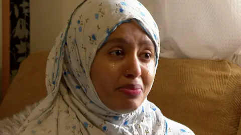 BBC Portrait shot of Shakila Meli, who is from Kenya, crying and wearing a white headscarf, with blue flower motifs 