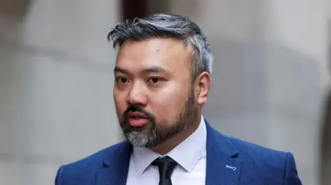 Reuters Defendant Chi Leung Wai, also known as Peter Wai, arrives at the Old Bailey, wearing a white shirt, dark tie and blue suit. He has a short salt-and-pepper beard and hair.