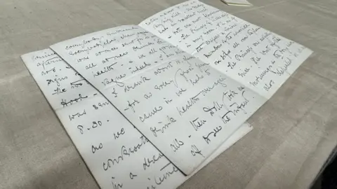 Two pages of handwriting on a beige linen surface.