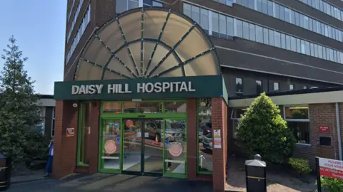 GOOGLE MAPS The entrance to a hospital. It says Daisy Hill Hospital in white over the doorway. There are sensor operated doors.