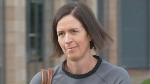 BBC Dr Kate Searle arrives for a hearing at a tribunal - she is wearing a grey top, has a brown handbag over their shoulder and has brunette hair