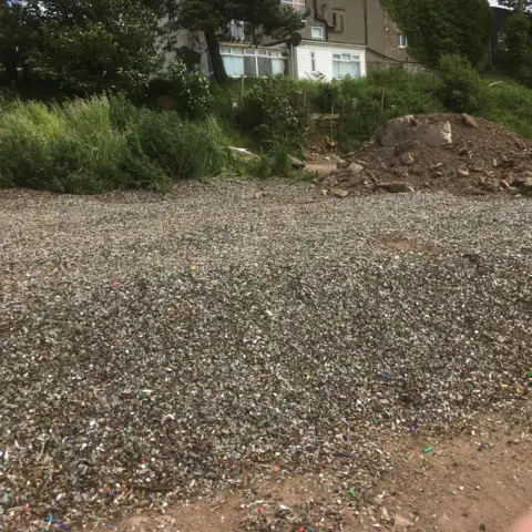 Supplied At the front of the image is a pile of what appear to be small fragments of waste, including glass and plastic. Behind this and to the right is a mound of earth