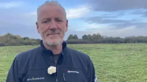 Jo Makel/BBC Head and shoulders shot of Paul Matson. He is standing on a field and is wearing black jacket with the Hull4Heroes emblem on it.