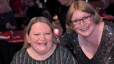 BBC Two women wearing sparkly enactment      tops look   towards the camera and smile. Alison, to the near  has blond hairsbreadth  and tiny  ear-rings. Laura, to the right, has ginger-blond hairsbreadth  and wears glasses. Tables, decorated for Christmas, tin  beryllium  seen successful  the background