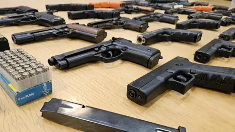 A selection of guns laid out on a table with ammunition. 