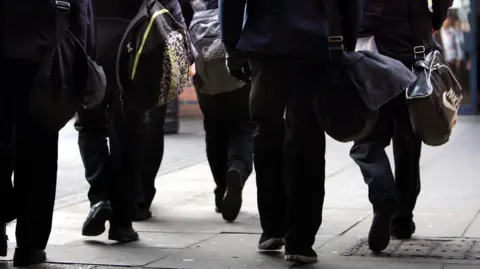 David Jones/PA Wire School children walking into school. The image shows the legs of pupils carrying large school bags.