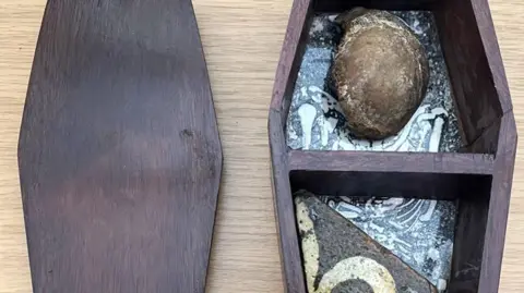 Image of a circular piece of knee bone and a section of tile in a small wooden box.
