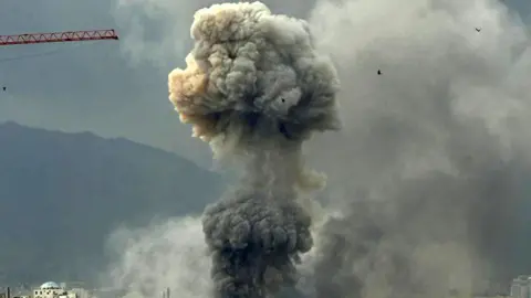 Supplied Smoke rising from above buildings in two clouds, one above the other. The boom of a red crane can be seen on the left.