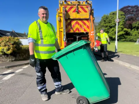 Disclosure reporter Kevin Keane about to load a green bin onto the refuse lorry while out on a collection with workers in Fife.