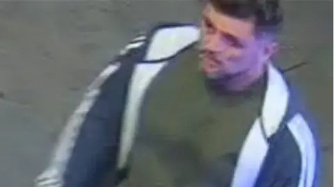 A CCTV image of a man wearing a green t-shirt and navy a white jacket.