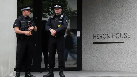 Ryan Jenkinson / Getty Images Two police officers stand in front of the entrance to a building with lettering that reads 'Heron House', in Manchester on 23 July.