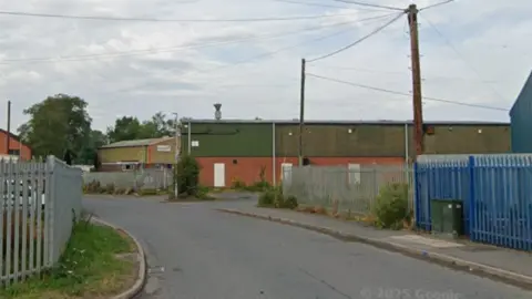 An industrial estate with metal fences and a narrow road