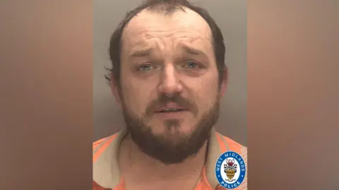 West Midlands Police Darren Coffey's mug shot. He has brown hair and facial hair and is wearing an orange and beige t-shirt on.