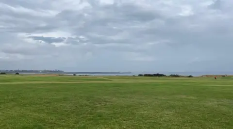 The Leas, along the coast road at South Shields. A grassy area lies in the foreground, with the sea in the distance and grey, stormy skies above.