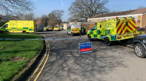 A road closed sign with police cars and ambulances parked on the street