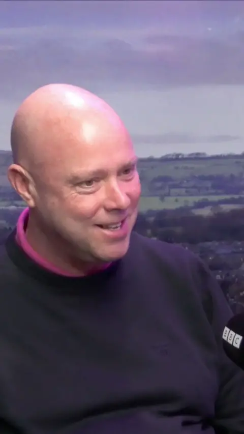 Bald headed man in a blue jumper in front of a lancashire landscape