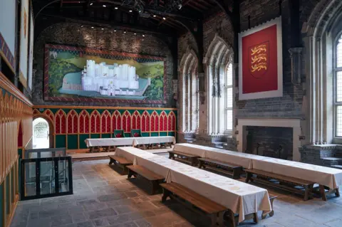 Cadw Great hall of Caerphilly castle, with long tables and tapestries on the wall