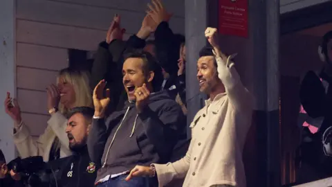 Action Images/Reuters Rob Mac and Ryan Reynolds celebrating a goal at a Wrexham football match. Rob is holding his fist in the air and Ryan is smiling with his mouth open, mid applause.