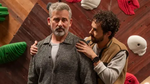 HBO Steve Carrell and Ramy Youssef star in Mountainhead - Carrell is on the left and is wearing a grey cardigan, Youssef has a beige top and light brown waistcoat on.