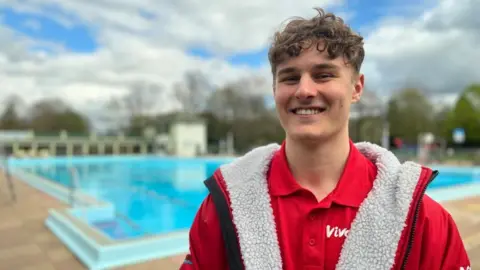 Emma Baugh/BBC Lifeguard Tom Jackson in red uniform smiling