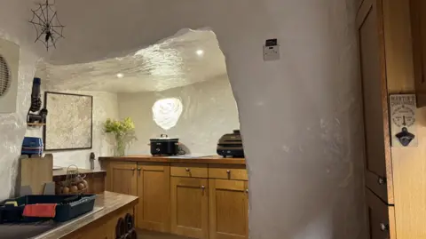 The kitchen also has white walls with a cave-like texture to them. The hob and cupboards are inside a slightly smaller section which has been carved into the wall.