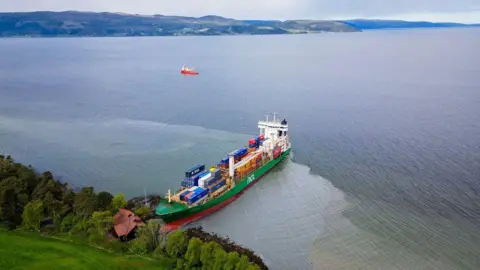 EPA A birds-eye view of the green ship, filled with containers, with the top of the boat on land, next to the house.