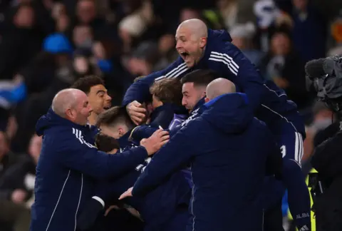 Action Images/Reuters Men in navy Scotland tracksuits hug, including Scotland manager Steve Clarke, with a stand full of fans in the background 