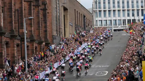 Reuters Dozens of cyclists going up Montrose Street during the men's elite road race at the UCI Cycling World Championships. The pavements are packed with people cheering them on, waving flags