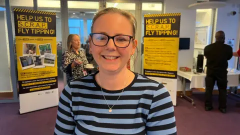 Nicola Tansley, the community protection lead officer for Chelmsford City Council, with two campaign posters behind her in the background saying "help us to scrap fly tipping!".