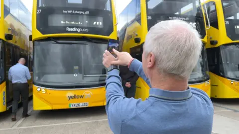 Cllr John Ennis the politician responsible for transport in Reading uses his phone to take a picture of one of the new yellow painted electric buses.