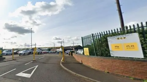 Google A Google street view image of the entrance to a car park with yellow barriers and several cars can be seen parked up. To the left of the car park is a sign that reads NCP with a yellow background.