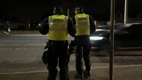 Two police officers in high-vis vests standing at the side of a road