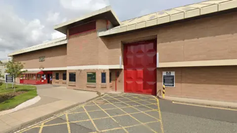 Google The outside of Holme House Prison which is a large brick building with a big red gate and smaller entrance to the left.