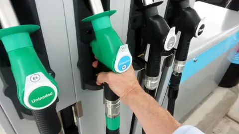 A close up image of a hand lifting a petrol pump from a row of pumps.