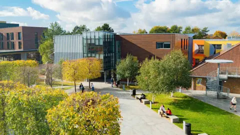 An aerial picture of Arts University Bournemouth's campus. Some students can be seen dotted around. There are several trees. The university building itself includes a central structure with a glass exterior.