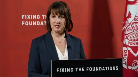 PA Media Chancellor Rachel Reeves giving a press conference behind a lectern which reads 