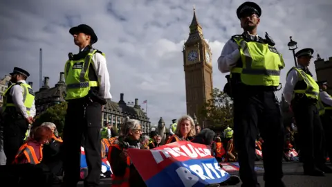 Reuters Police officers standing around Insulate Britain activists who are blocking a road outside the Houses of Parliament in a sit-down protest