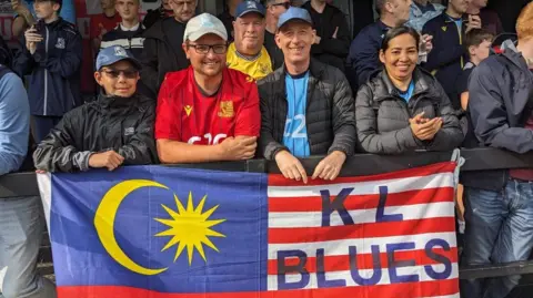 Mike Jolly A man and his wife and two other people holding a blues flag to show their support for their team.