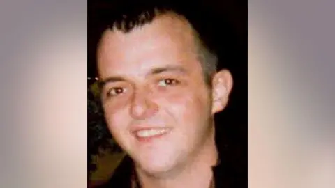 Head shot of Michael Lyons, who is wearing a jacket with a black collar. He is smiling and looking at the camera. He has short black hair, combed forward.