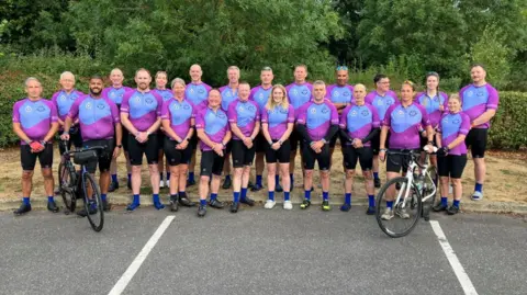 James Grant/BBC A group of people in pink and blue jerseys line up posing for a photo. 