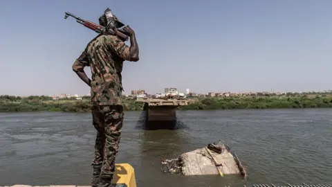 Getty Images A view of the back of a soldier in camouflage holding a gun over his shoulder. He is looking at a broken bridge over the Nile.