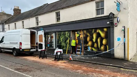 Two men working on a Co-op building behind police tape