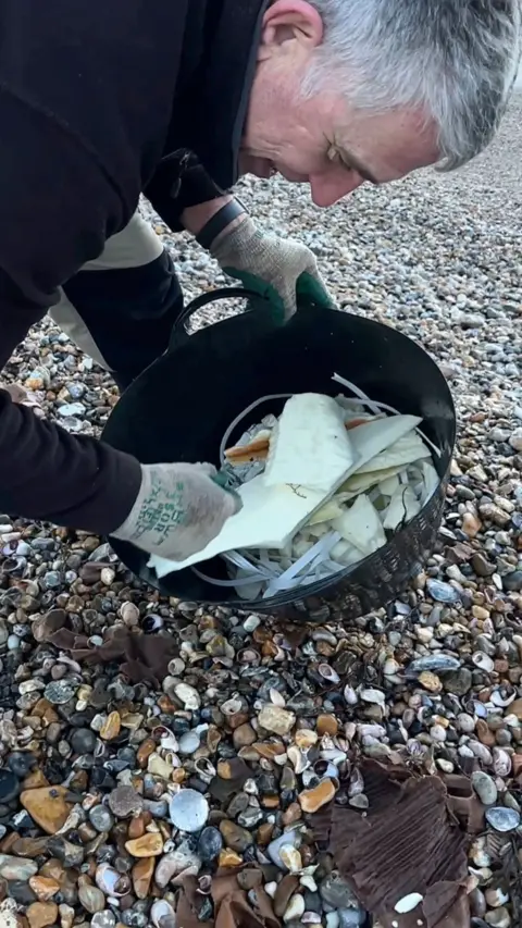A man putting things into a bucket on the beach.