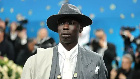Man in top hat stands on red carpet