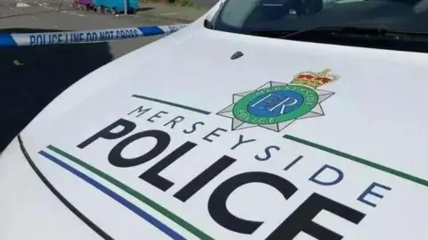 The bonnet of a Merseyside Police patrol car, with the force's badge and name painted onto a white background.