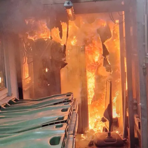 Leicestershire Fire and Rescue Service Fire raging inside a building viewed through an alleyway past a row of Biffa bins