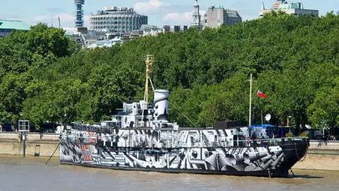 Getty Images A large sloop, moored to the side of an embankment. It is painted in black and white zigzags and shapes.