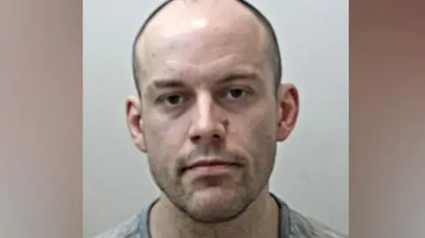 Matthew Matthiason's mugshot. He is balding with very short dark hair and stubble