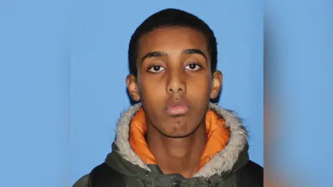 Northamptonshire Police A head and shoulders shot of Waijs Dahir taken against a blue background. He is wearing a green winter coat with an organge and faux fur lining.