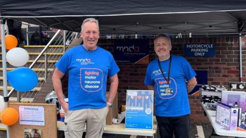 Two fundraisers wearing a blue t-shirt which says fighting motor neurone disease.
